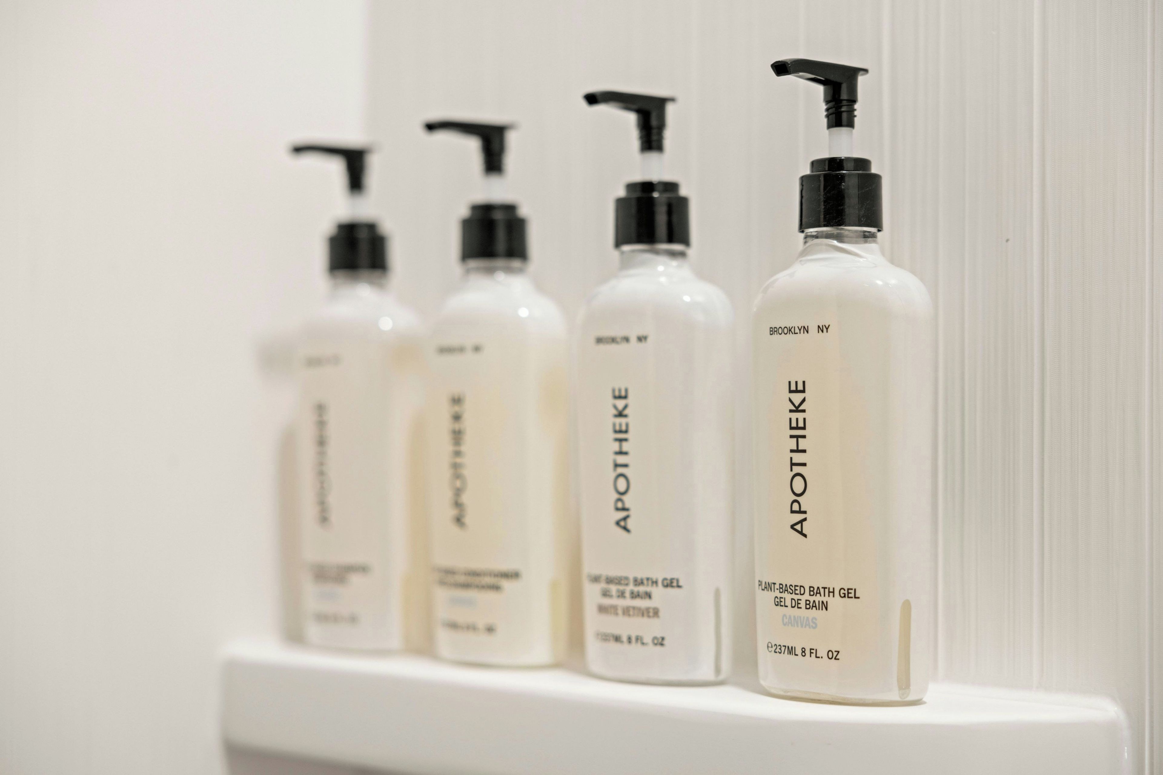 Four bottles of bath gel on a white shelf.