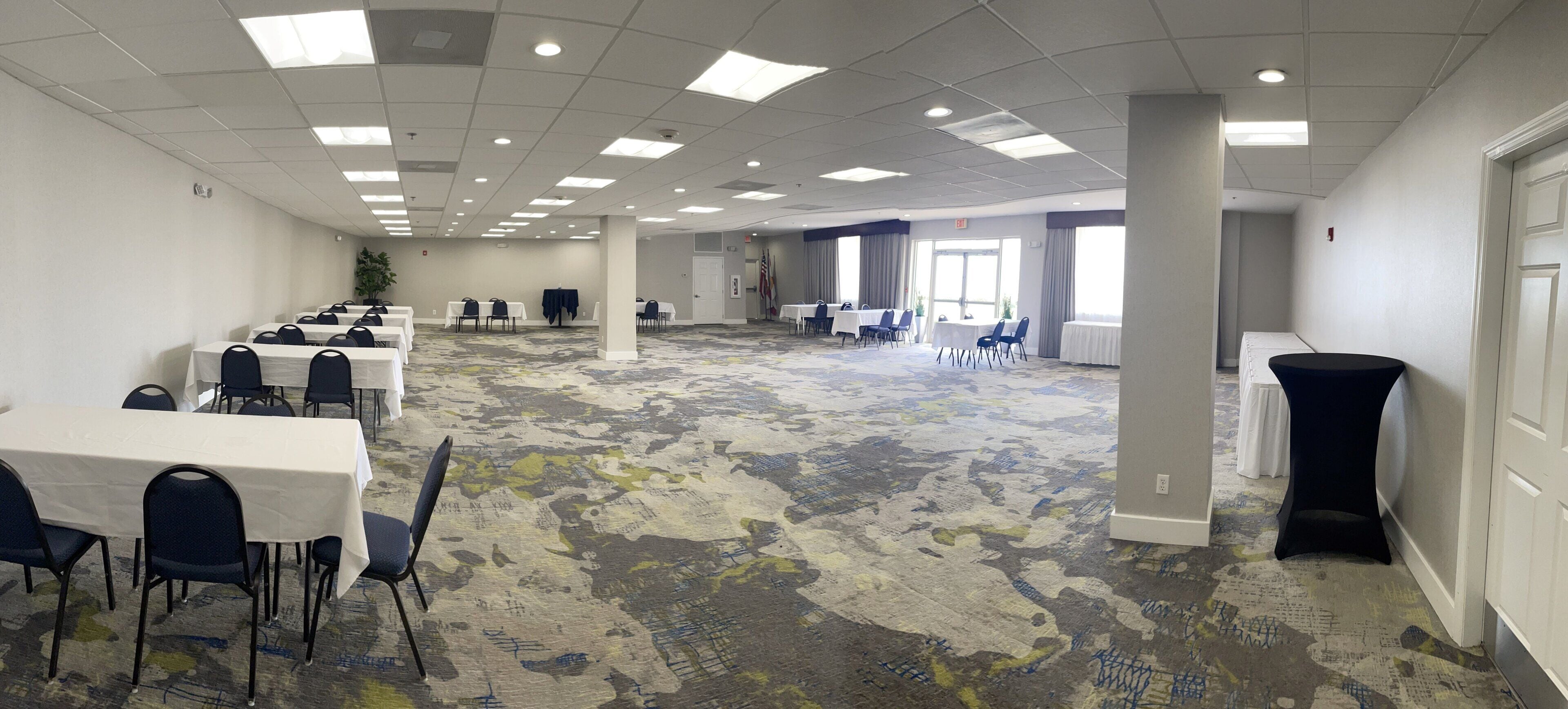Un salón de conferencias con mesas, sillas y piso alfombrado.