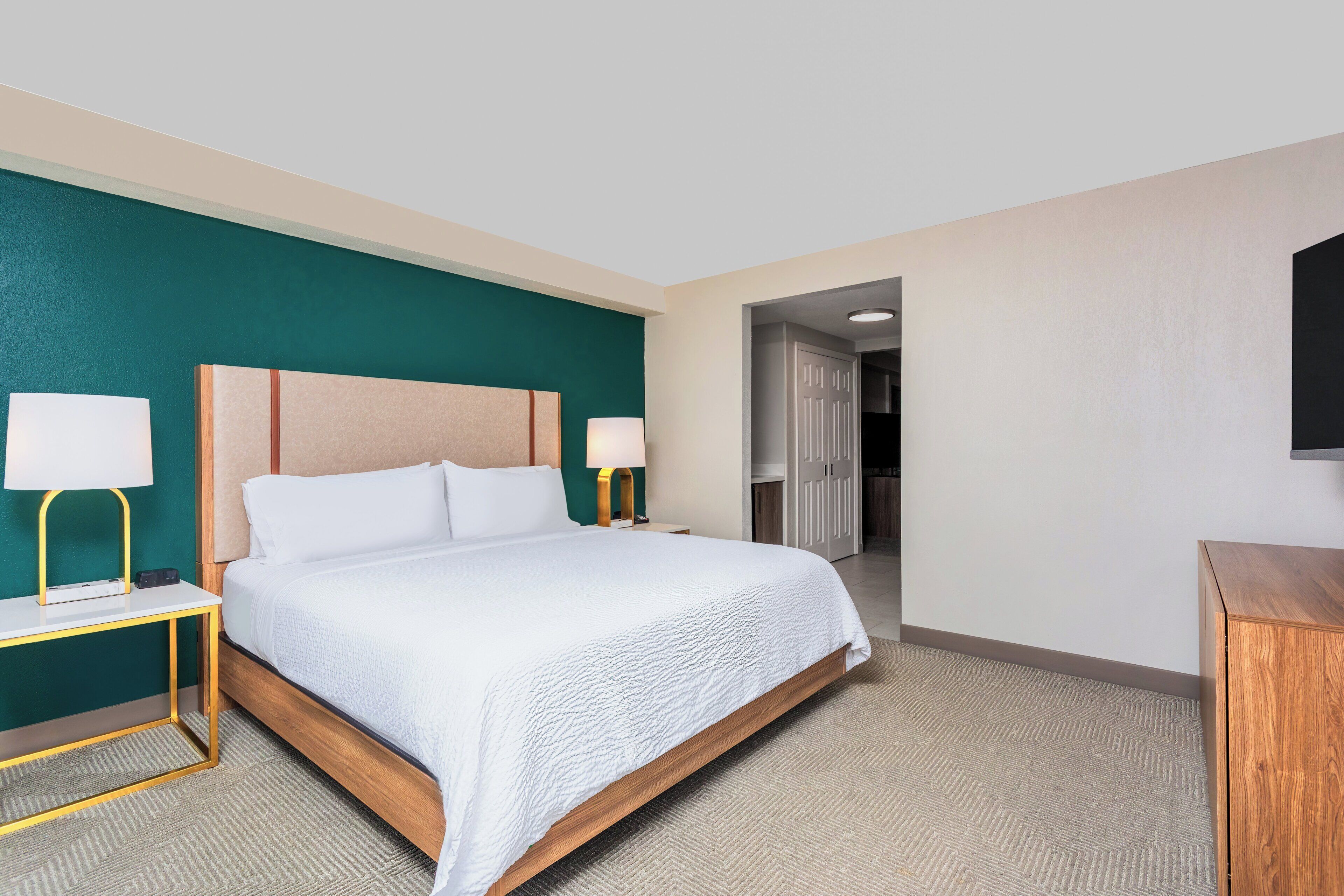 A hotel room with a bed, two bedside lamps, a nightstand, a wooden headboard, and a television on the wall.