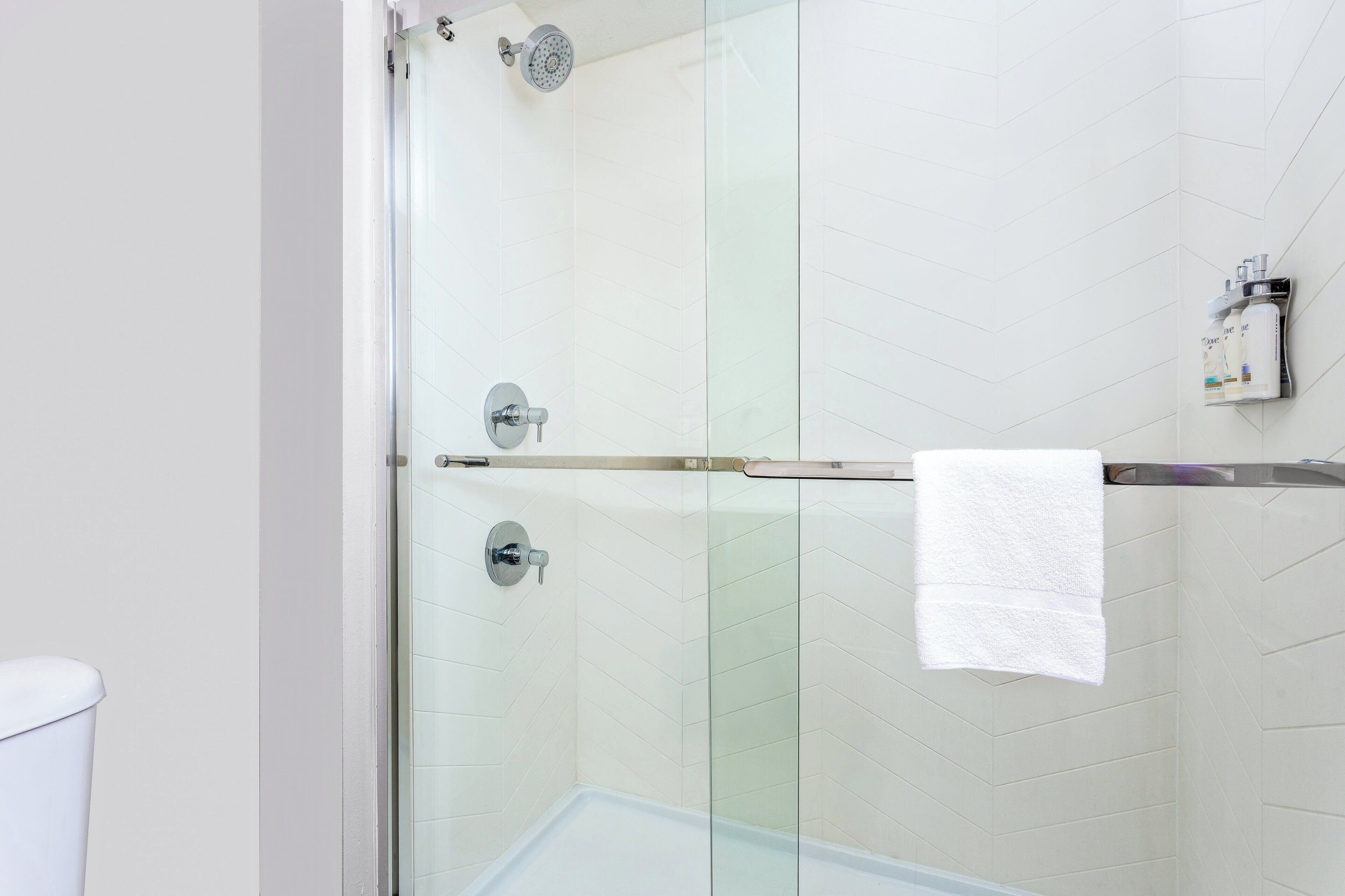 Een moderne badkamer met een glazen douchecabine, een witte handdoek aan een rek, en een toilet links.