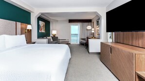 Ett hotellrum med en stor säng, ett skrivbord, en stol, en TV och utsikt över omgivningarna.