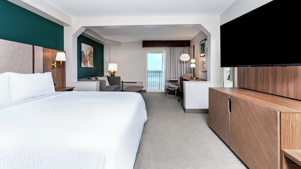 Habitación de hotel con una cama grande, un escritorio, una silla, un televisor y vistas al exterior.