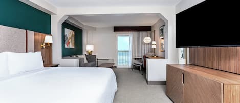 A hotel room with a large bed, a desk, a chair, a TV, and a view of the outdoors.