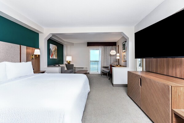 A hotel room with a large bed, a desk, a chair, a TV, and a view of the outdoors. - Holiday Inn & Suites Daytona Beach on the Ocean by IHG (Daytona Beach)
