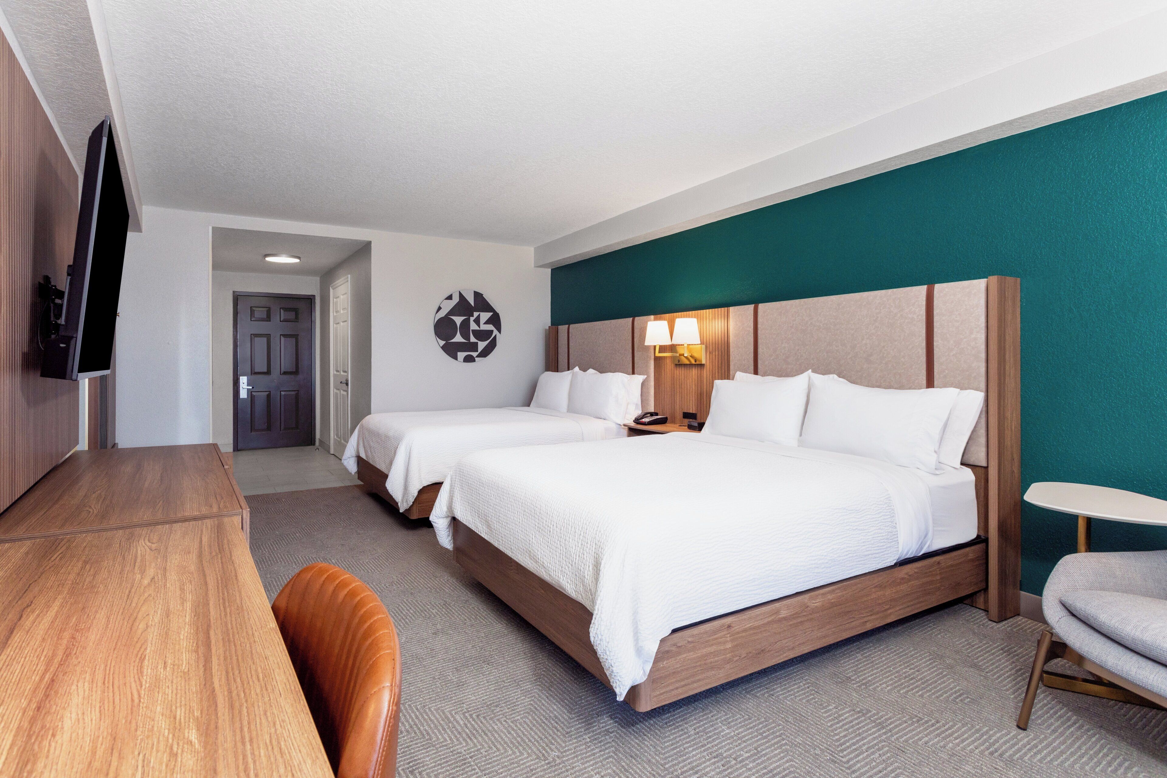 Ein Hotelzimmer mit zwei Betten, einem Schreibtisch, einem Fernseher und einem kleinen Tisch.