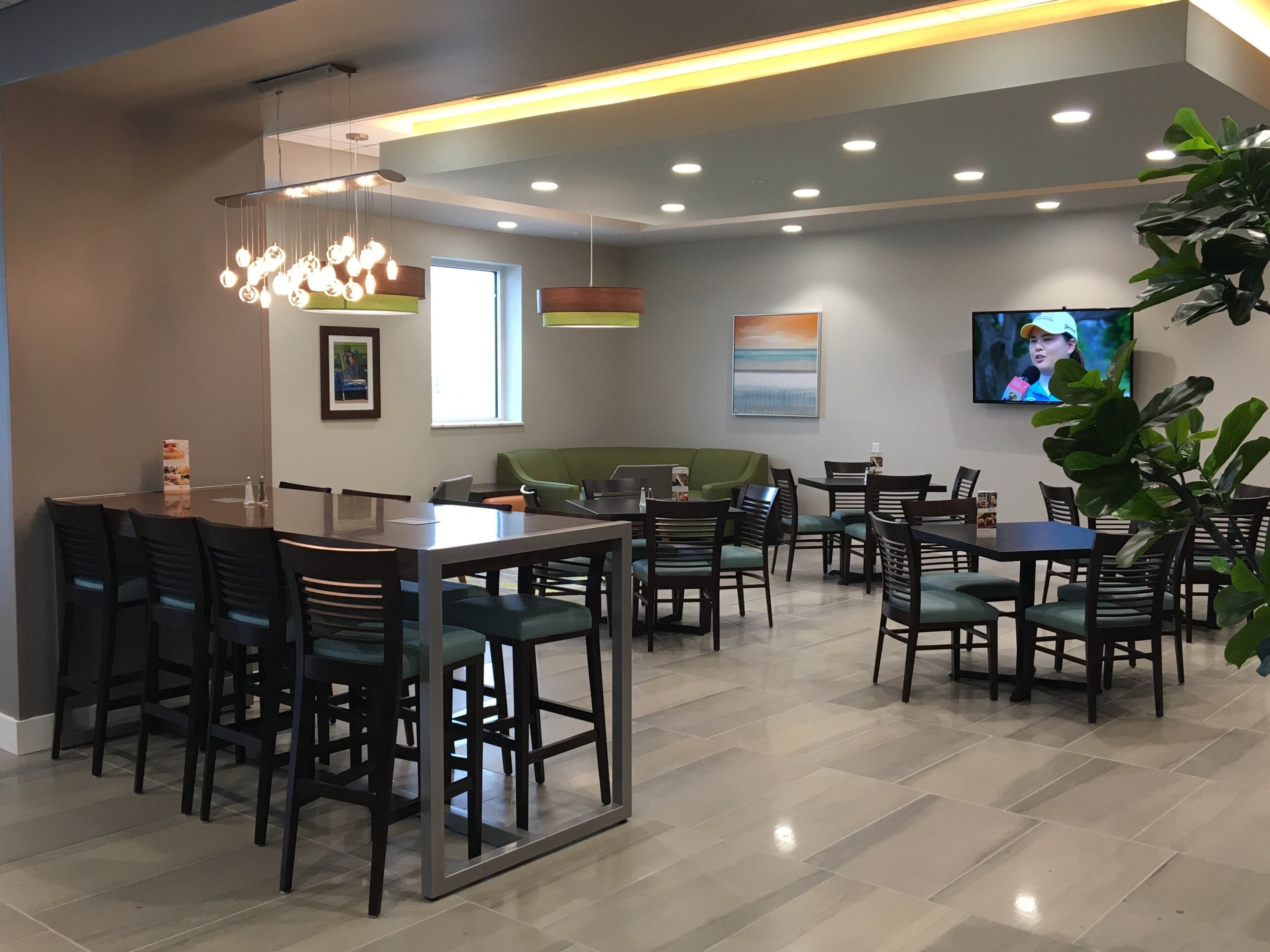 A modern dining area with a mix of tables and chairs, a green sofa, and a television screen.