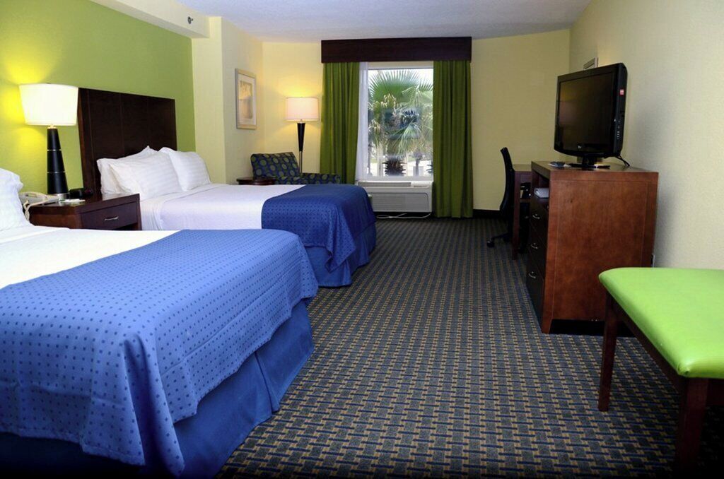 A hotel room with two beds, a desk, a television, and a window with curtains.