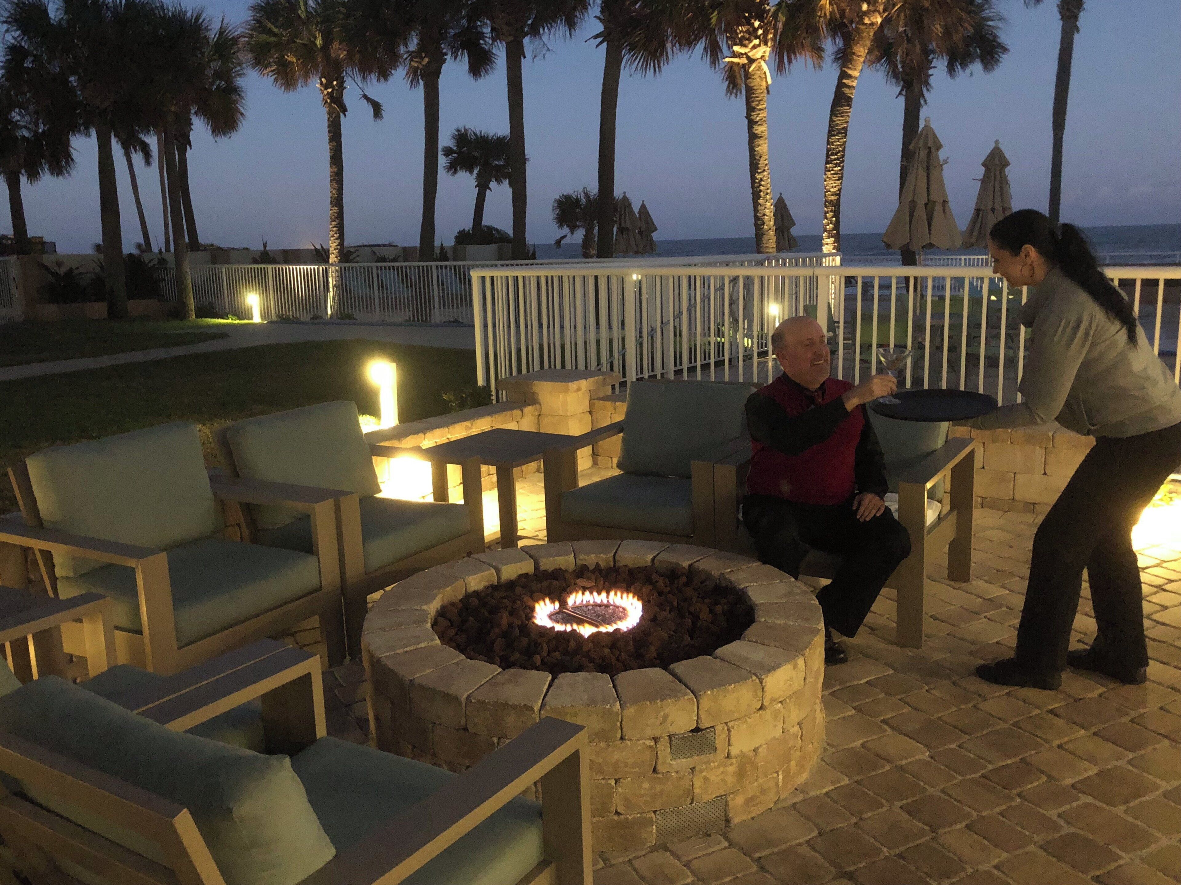 Un área de estar al aire libre con una chimenea, sillones reclinables y vistas al océano.