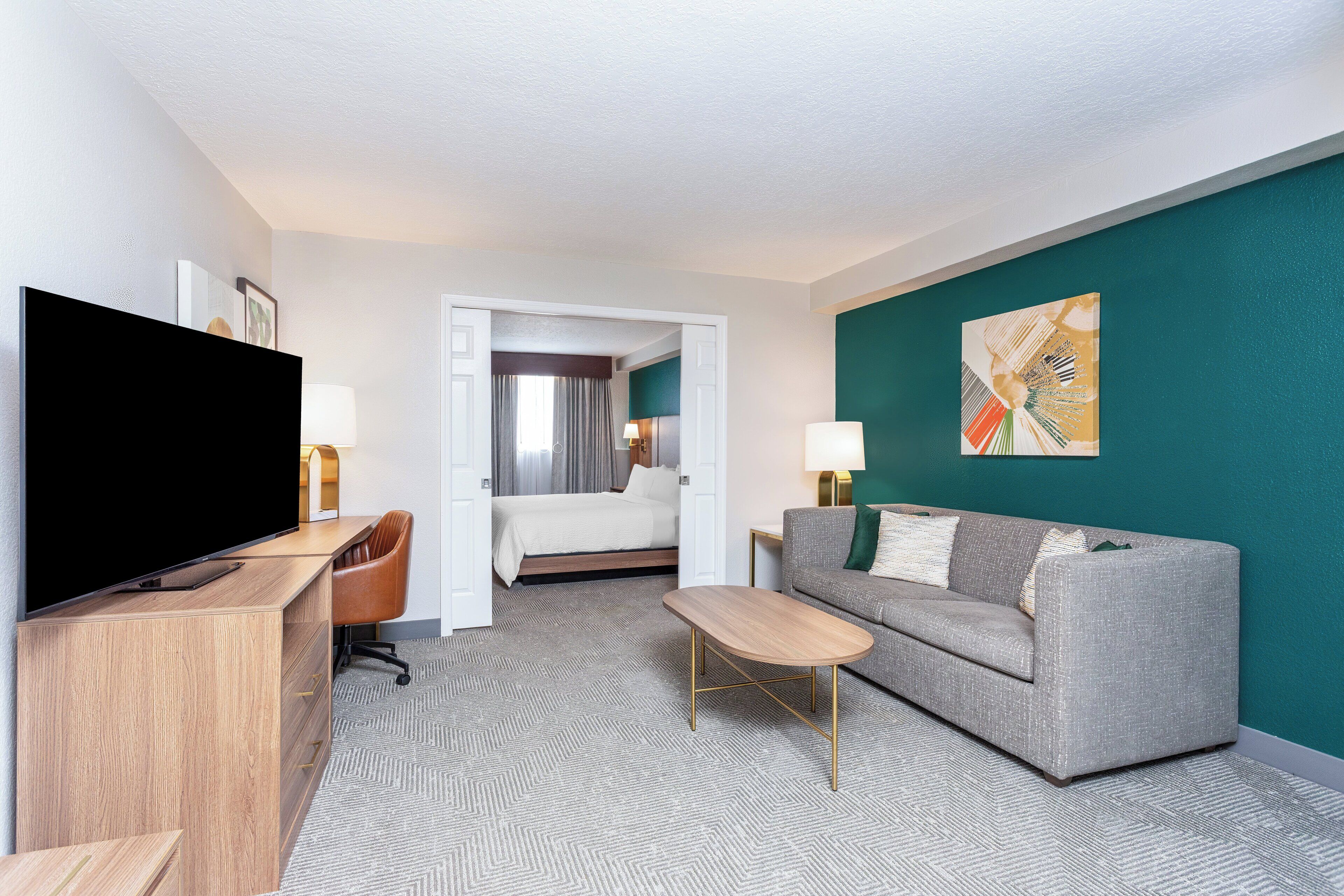 Ein Hotelzimmer mit Flachbildfernseher, einer Couch, einem Couchtisch und einem Bett.