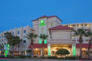 Un hotel Holiday Inn con una torre central, varios balcones y palmeras.