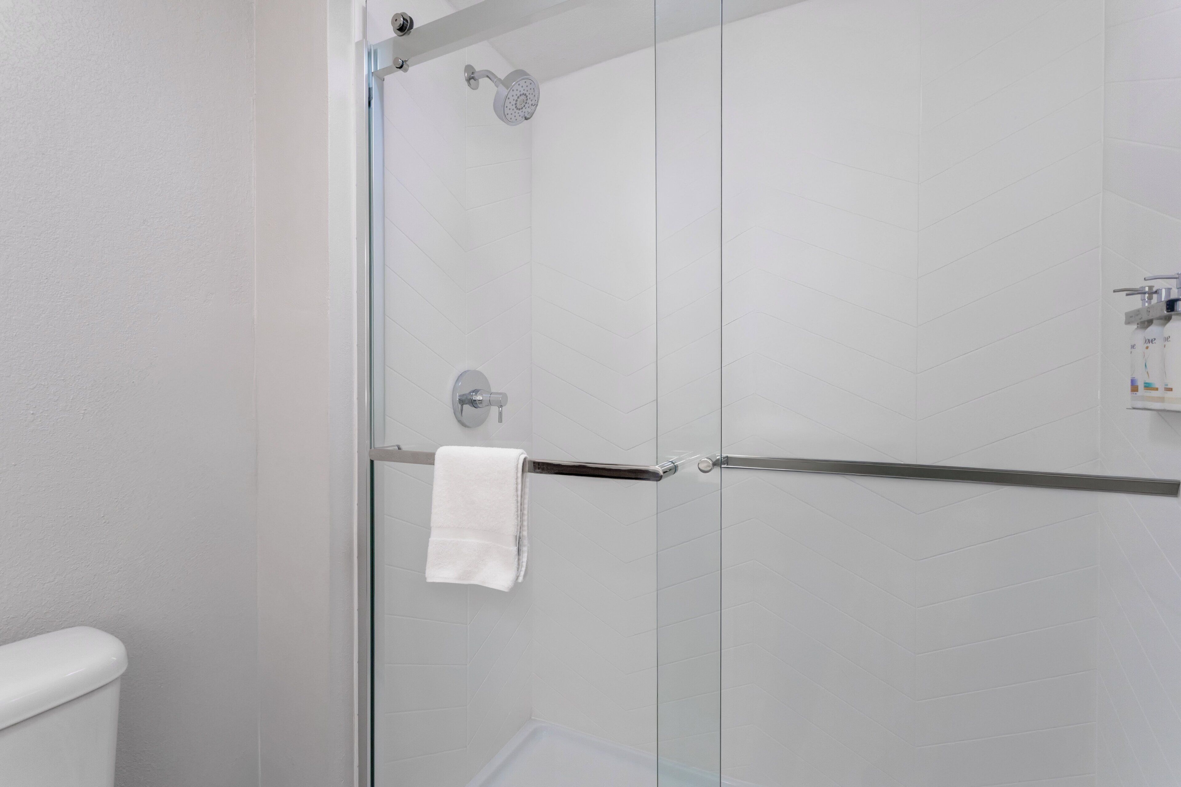 A modern bathroom with a glass shower enclosure, a white towel hanging on a metal rack, and a white tiled wall.