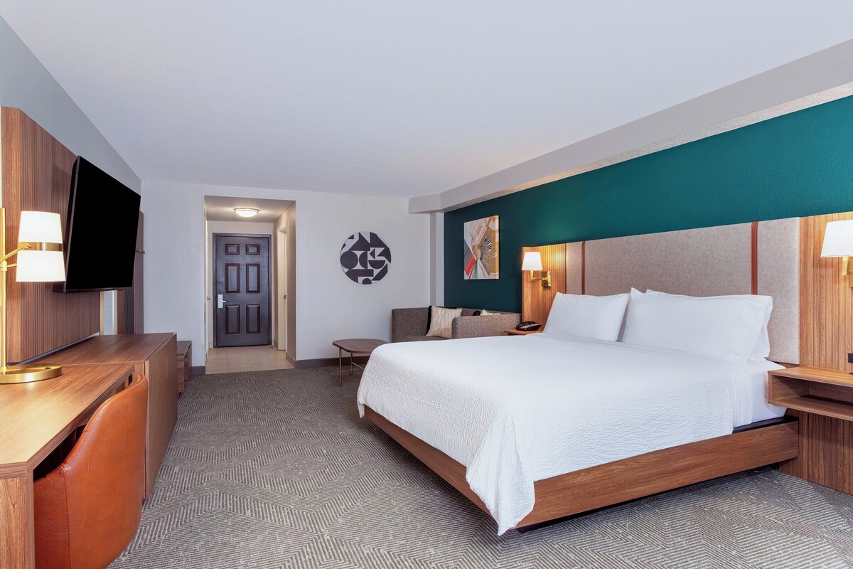 Een hotelkamer met een bed, bureau, televisie en een deur.