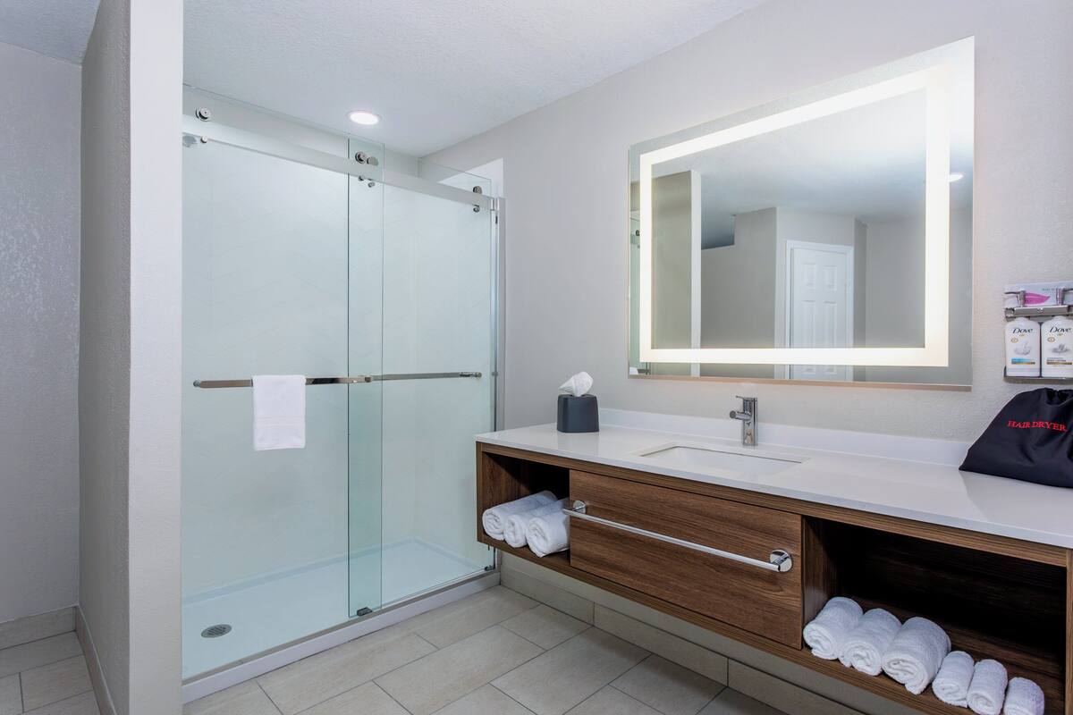 Een moderne badkamer met een douchecabine van glas, een grote spiegel en netjes opgevouwen handdoeken.