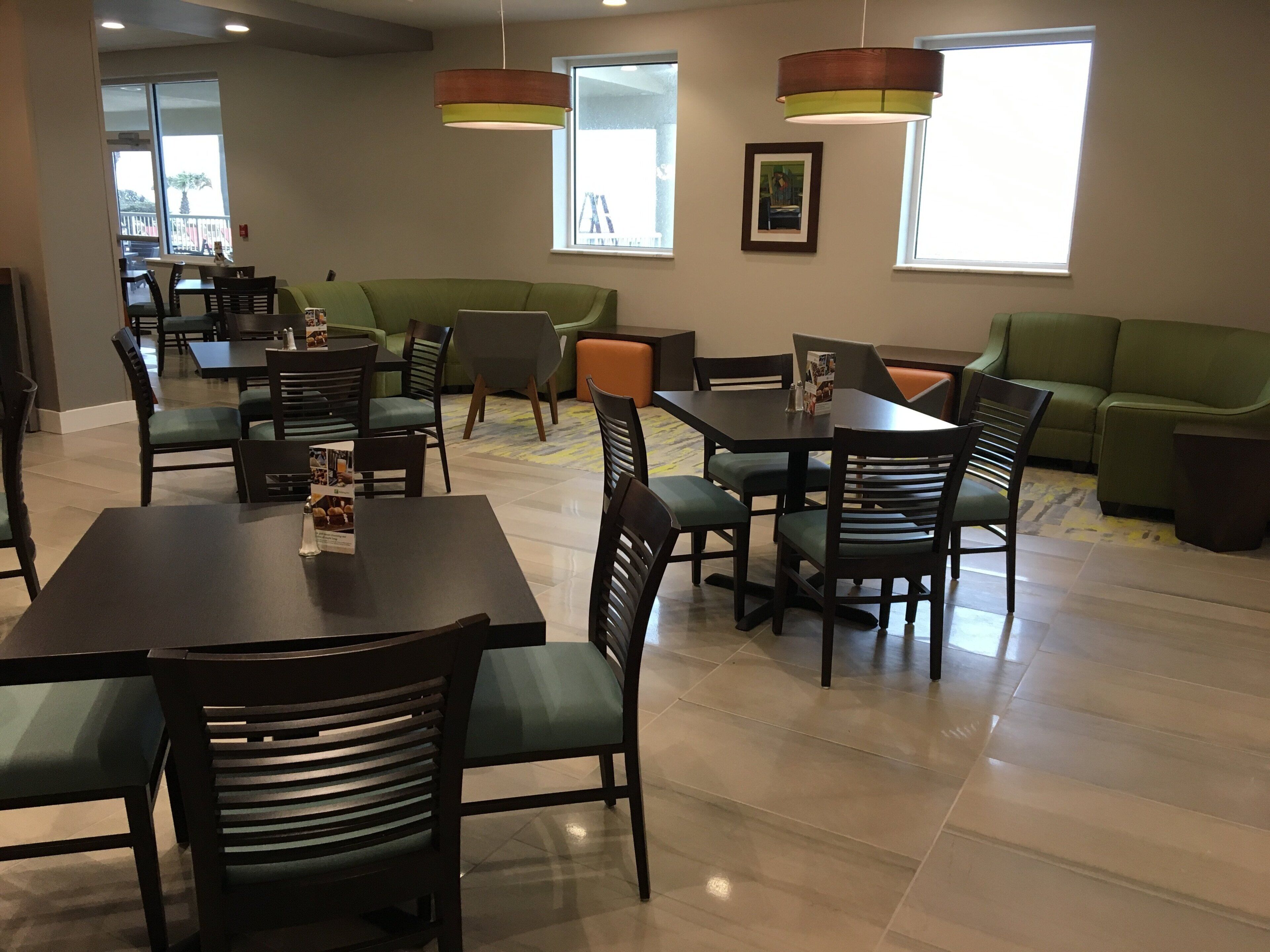 Un área de comedor con mesas y sillas, un sofá verde e iluminación colgante.