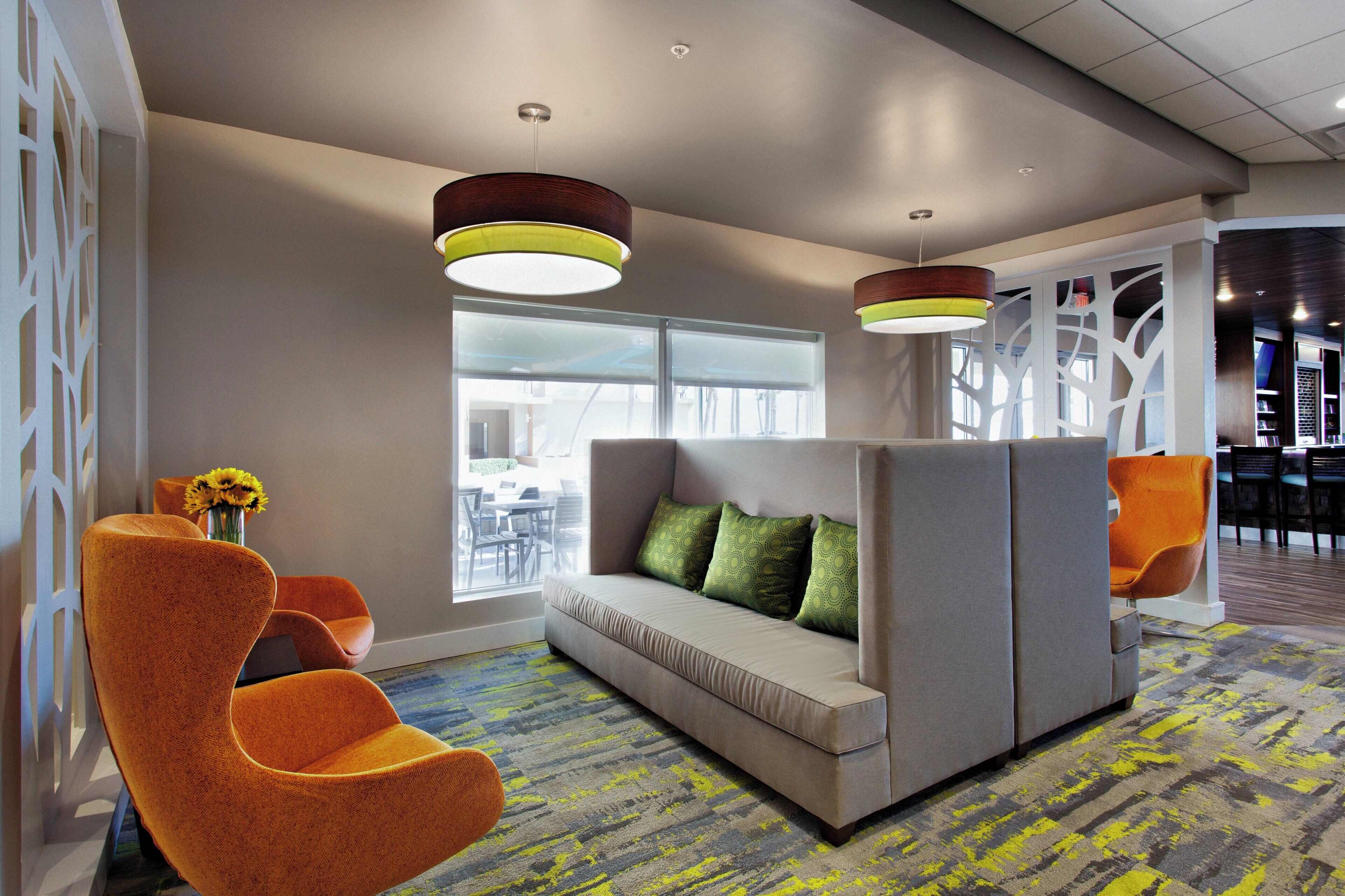 A modern lounge area with a sofa, orange chairs, and a patterned carpet.