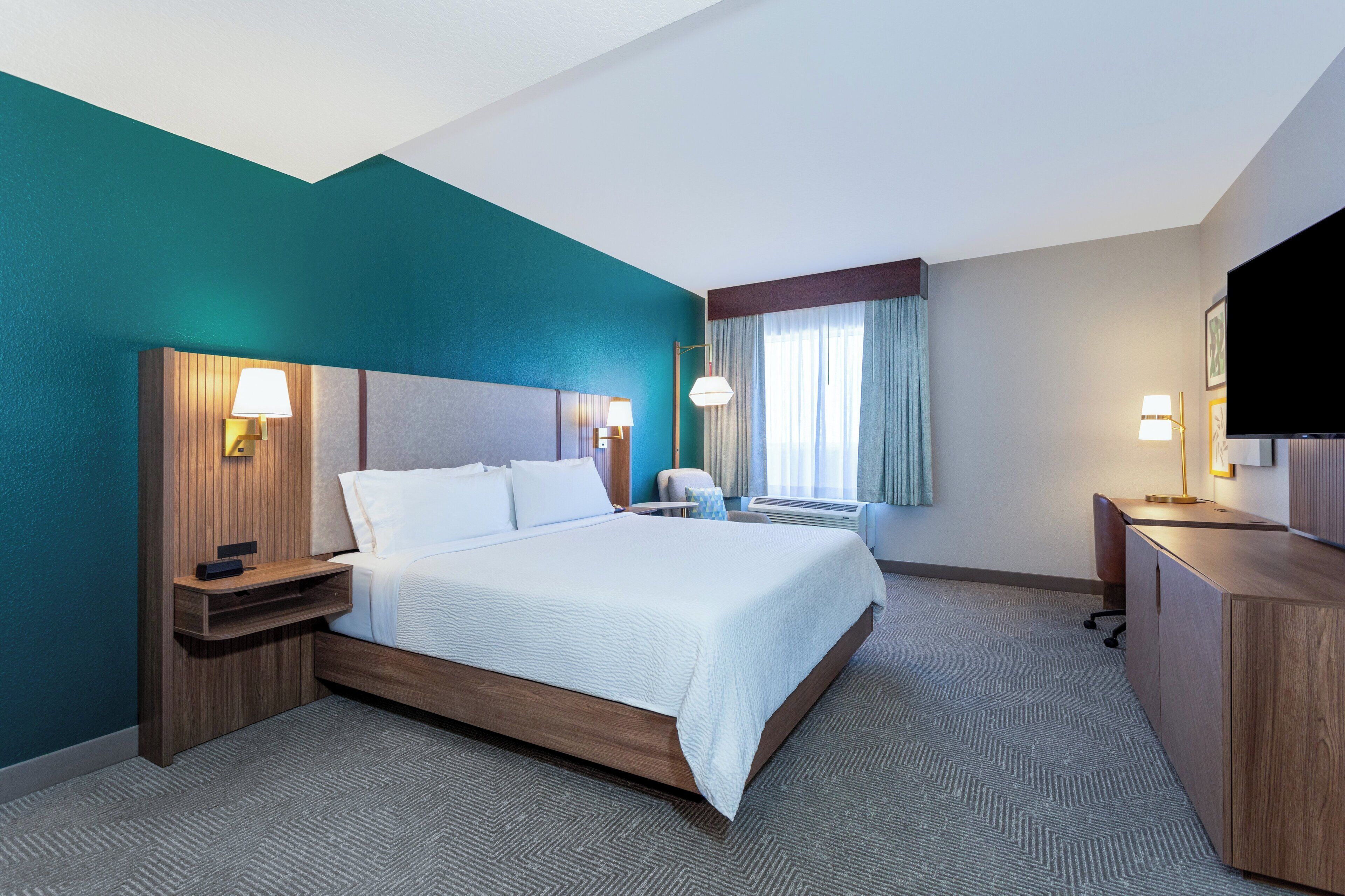 A hotel room with a bed, bedside tables, a desk, and a television.