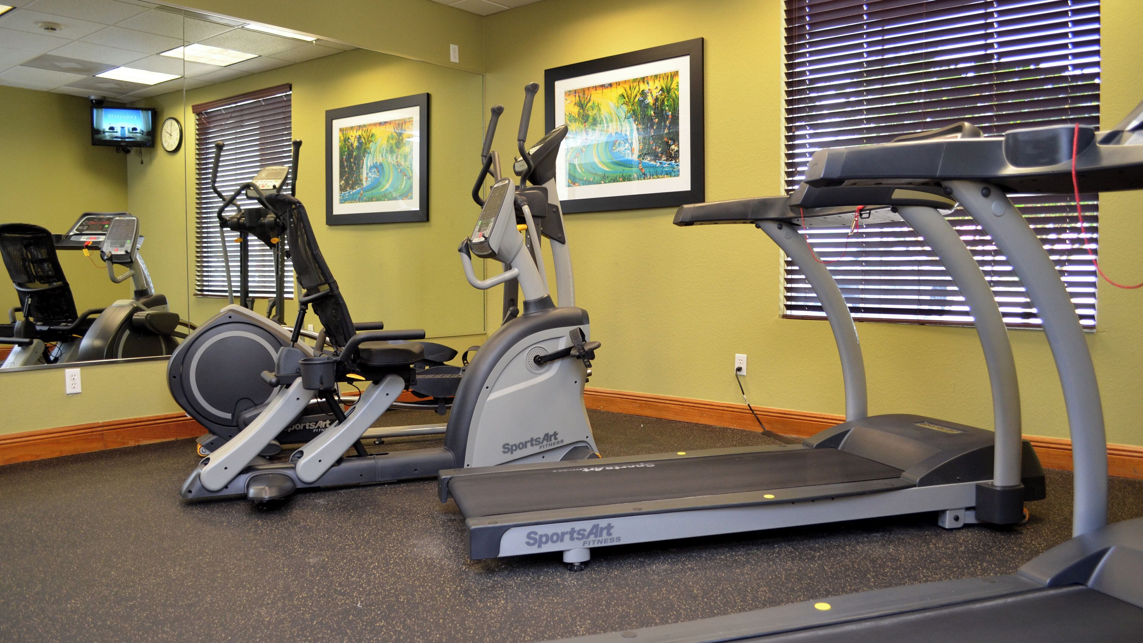 A fitness center with various exercise machines, including treadmills and stationary bikes, and a wall-mounted television.