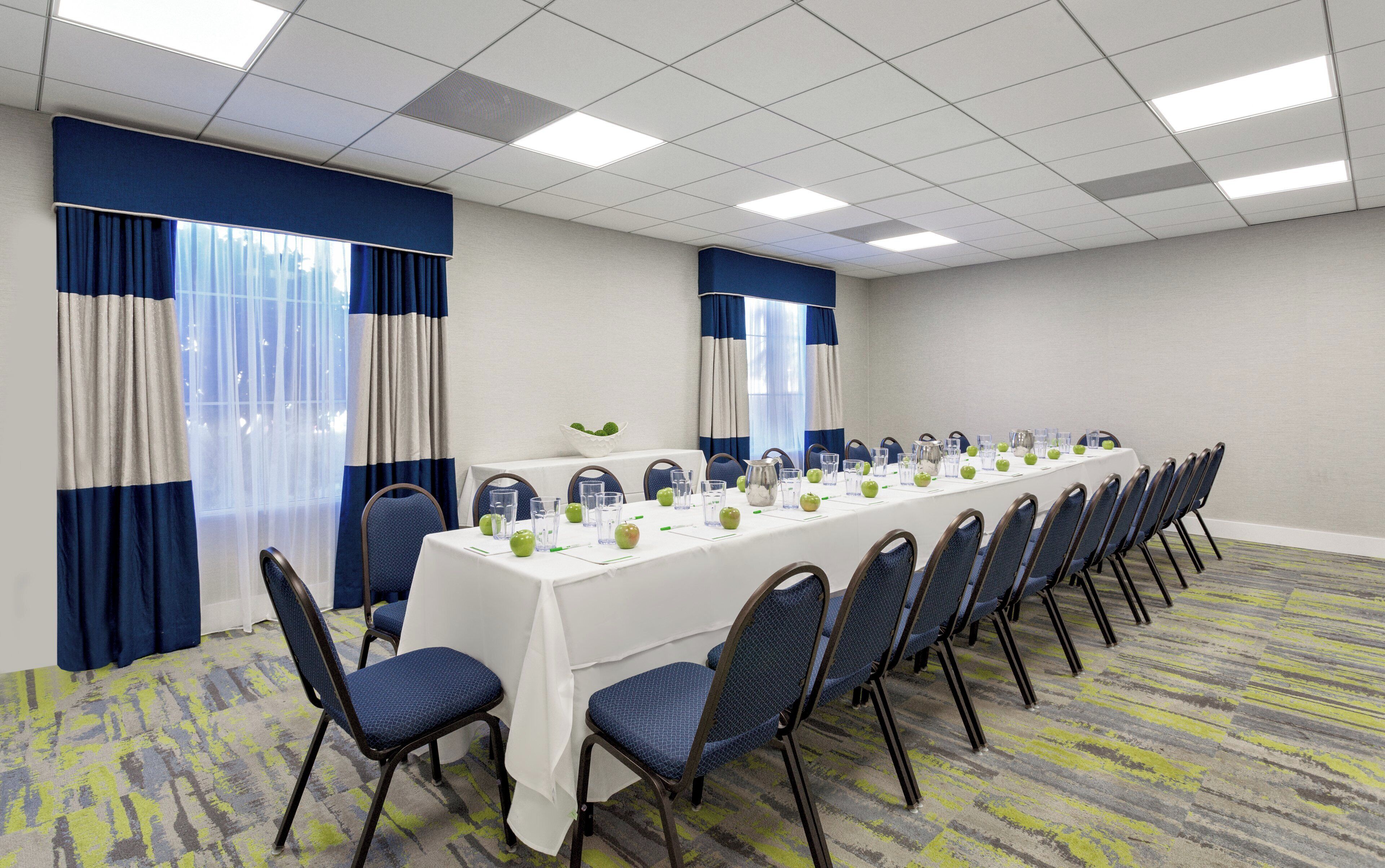 Une salle de conférence avec une longue table préparée pour une réunion, des chaises alignées de part et d’autre, et un sol recouvert de moquette.