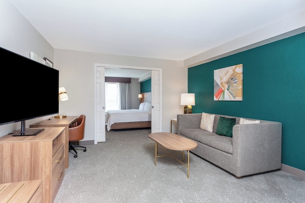 Ett hotellrum med en säng, ett skrivbord med en dator, en soffa och en tv.