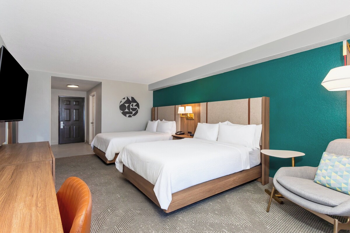 Hotelkamer met twee bedden, een bureau, een stoel, een televisie en een lamp.