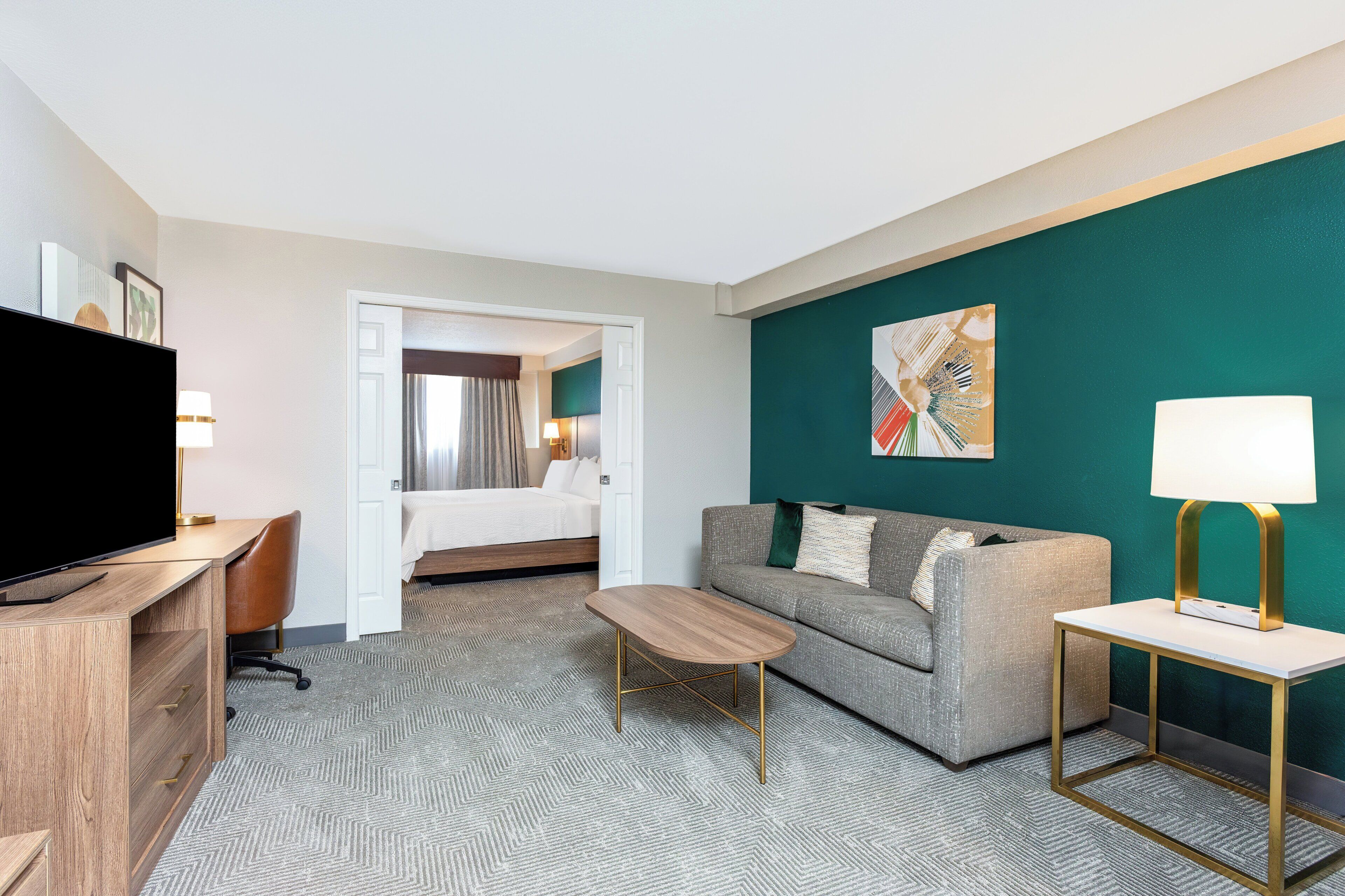 Una habitación de hotel con cama, escritorio, televisión, sofá y mesa de centro.