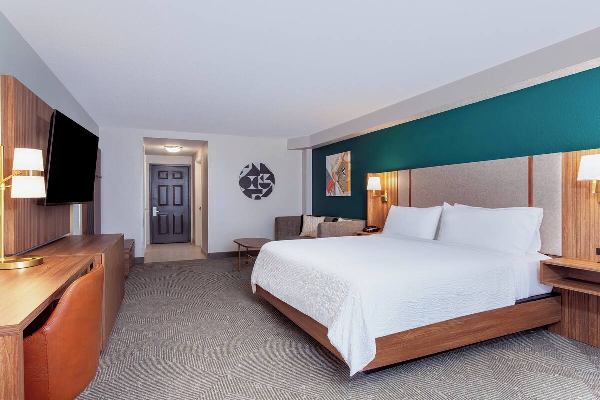 Een hotelkamer met een bed, bureau, televisie en een deur.