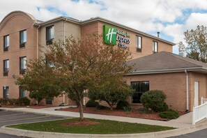 A Holiday Inn Express hotel with a brick facade, a green sign, and a tree in the front yard.