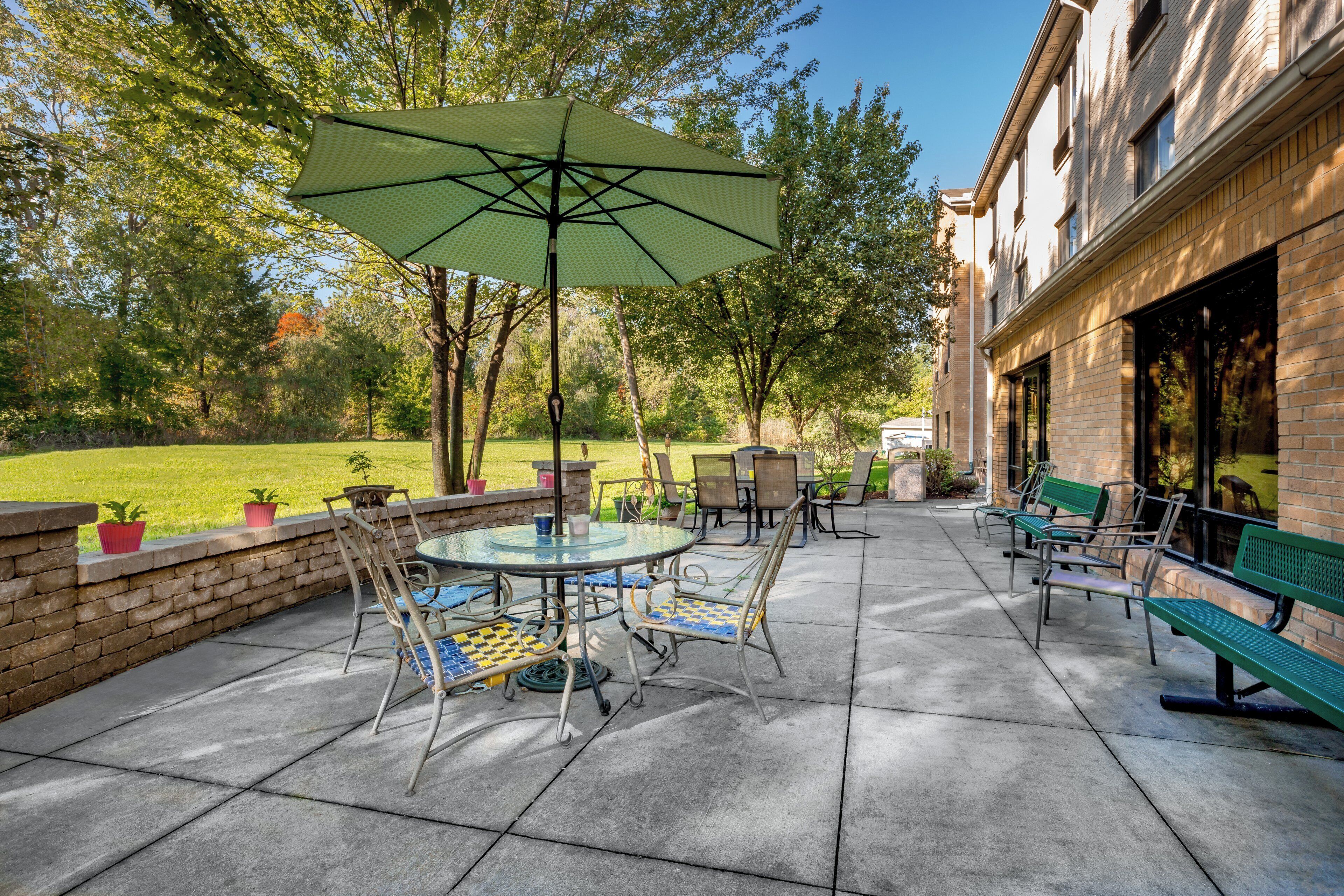 An outdoor patio with a round table, chairs, and a green umbrella.