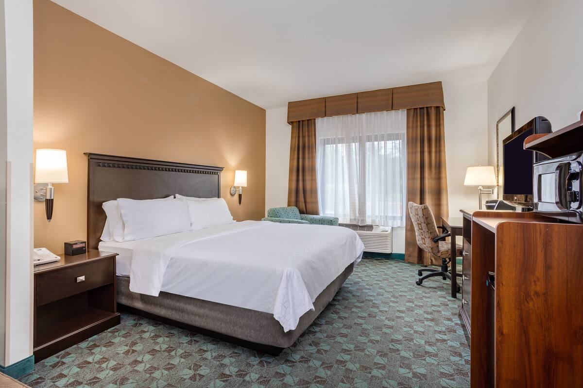 A hotel room with a large bed, a desk, a chair, and a television.