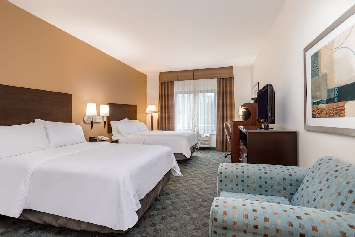 A hotel room with two beds, a desk, a chair, and a large window with curtains.