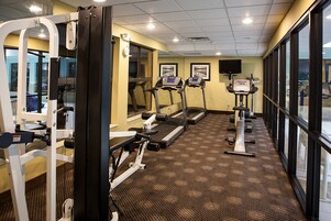 Un gimnasio con cintas de correr, equipo de ejercicio y ventanas amplias.