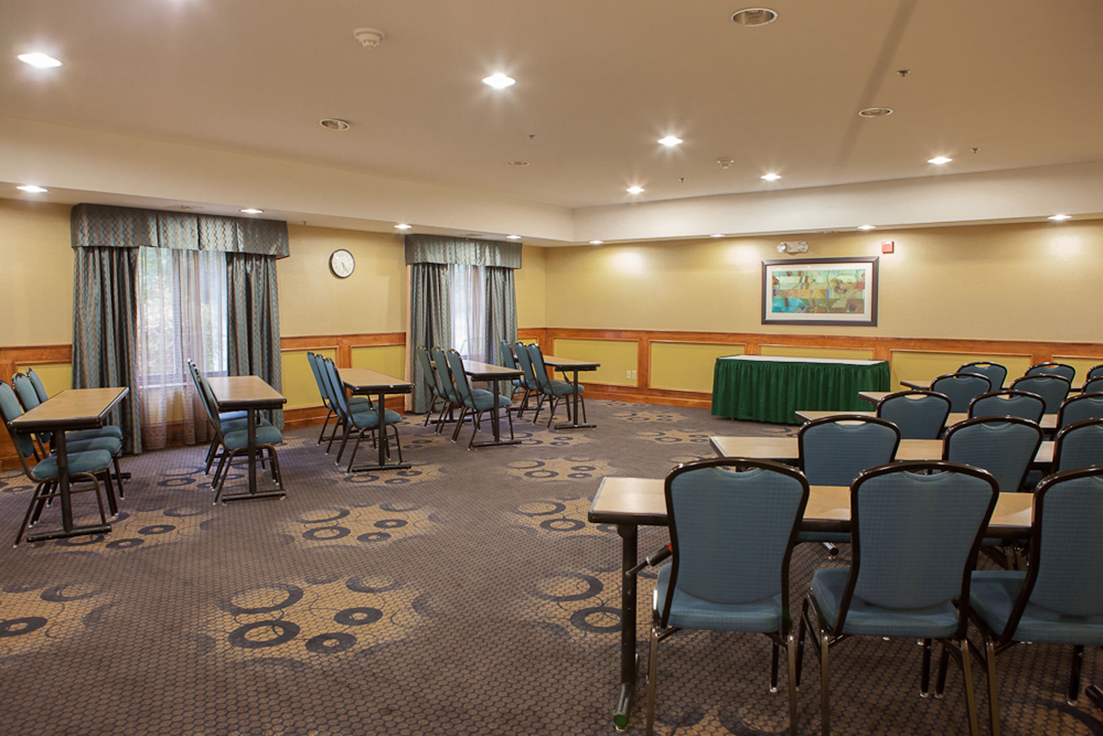A conference room with tables and chairs, a clock, and a painting on the wall.