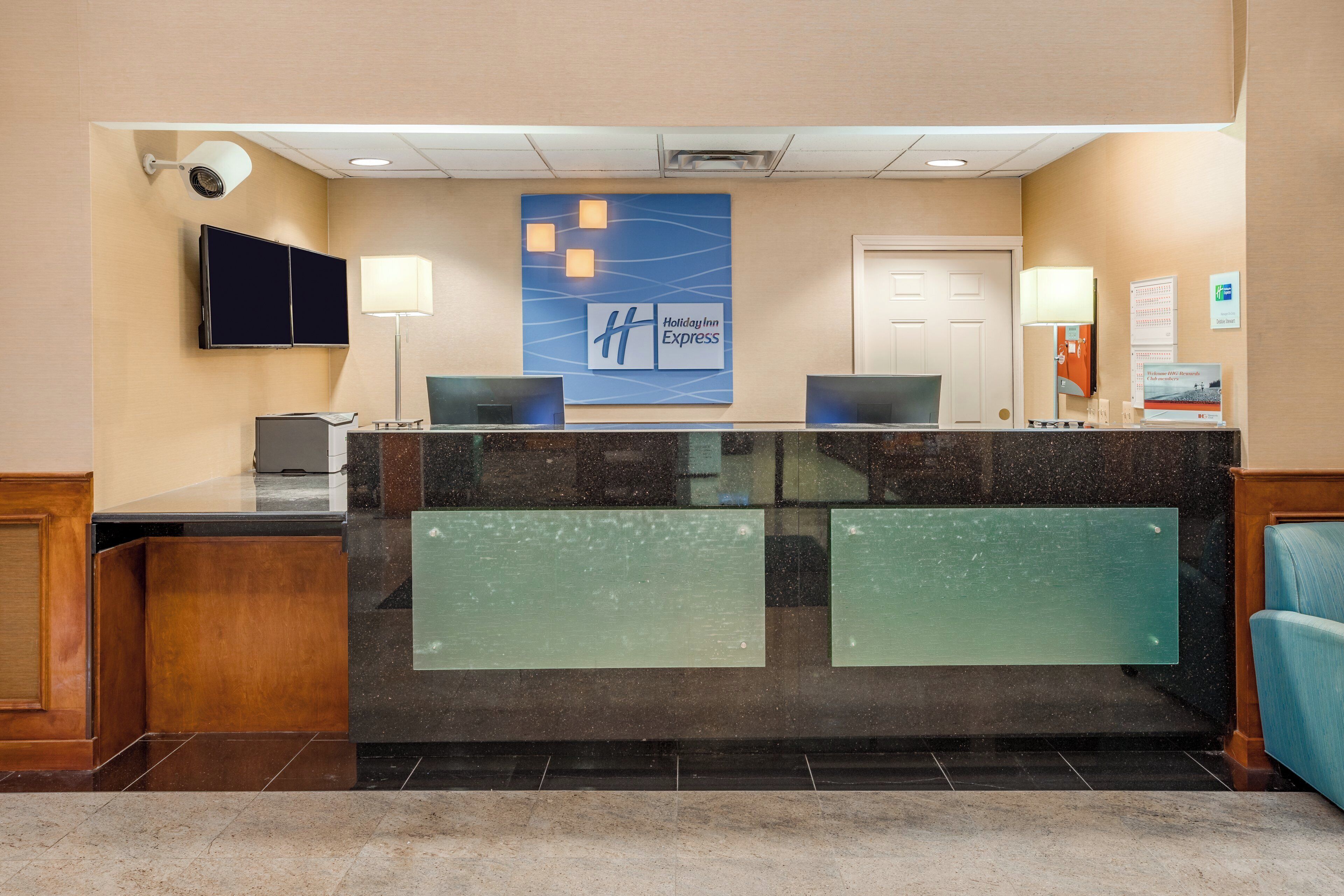 A hotel reception desk with a Holiday Inn Express sign, a flat-screen TV, a desk lamp, and a computer.