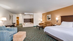 A hotel room with a large bed, a sofa, a chair, a small table, a lamp, a nightstand, and a bathroom with a bathtub and shower. - Holiday Inn Express Hotel & Suites Canton by IHG (Canton)