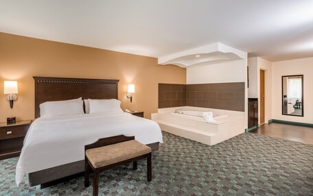 A hotel room with a large bed, a bench, a bathtub, and a small desk with a lamp.