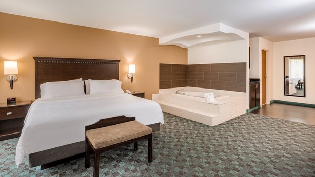 A hotel room with a large bed, a bench, a bathtub, and a small desk with a lamp. - Holiday Inn Express Hotel & Suites Canton by IHG (Canton)