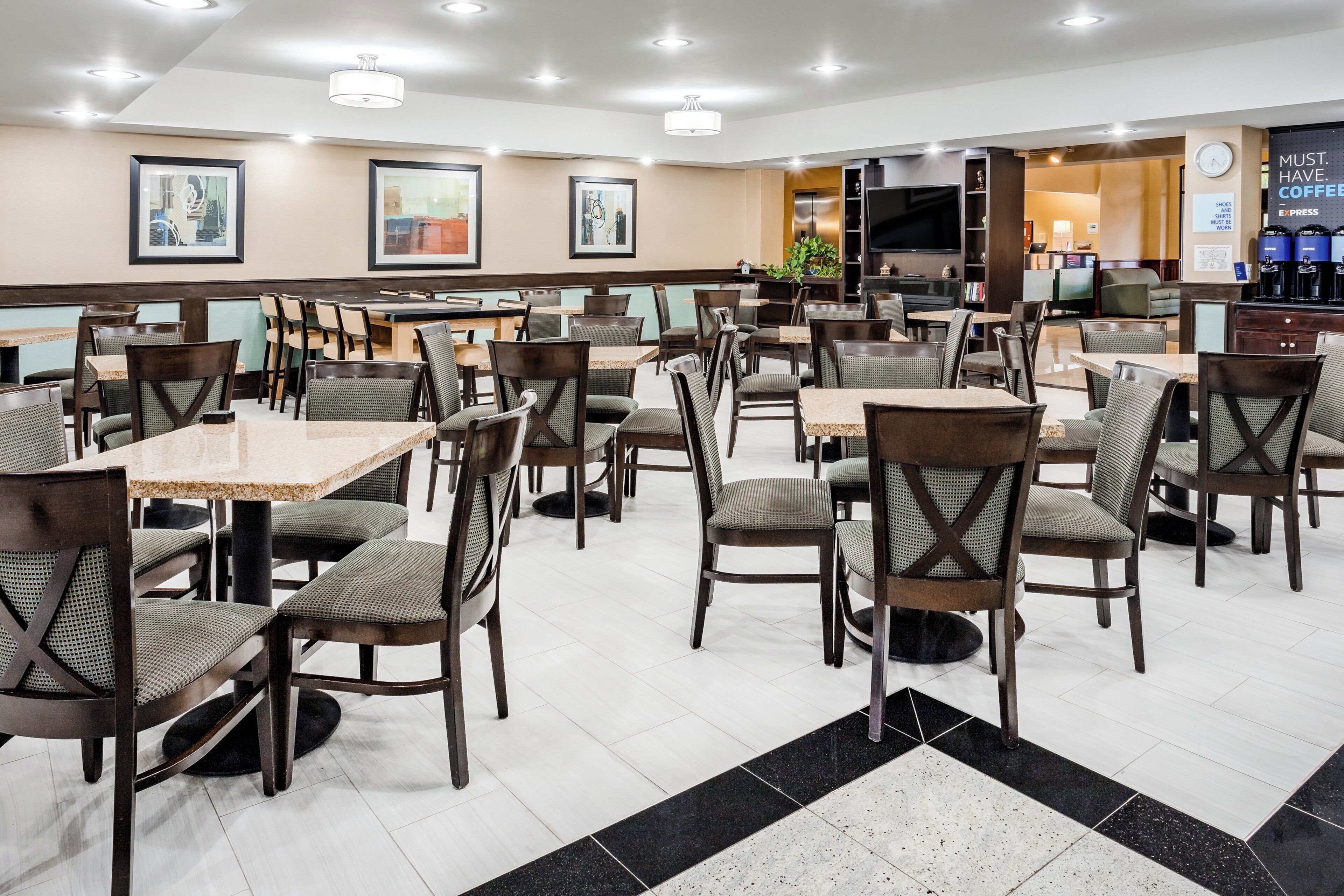 Ein Speisebereich eines Hotels mit mehreren Tischen und Stühlen, einem Flachbildfernseher und einer Kaffeestation.