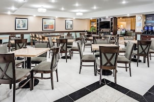A hotel dining area with multiple tables and chairs, a flat-screen TV, and a coffee station.