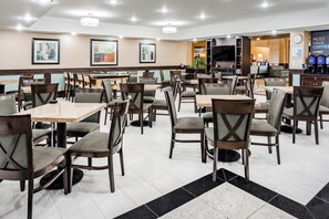 A hotel dining area with multiple tables and chairs, a flat-screen TV, and a coffee station.