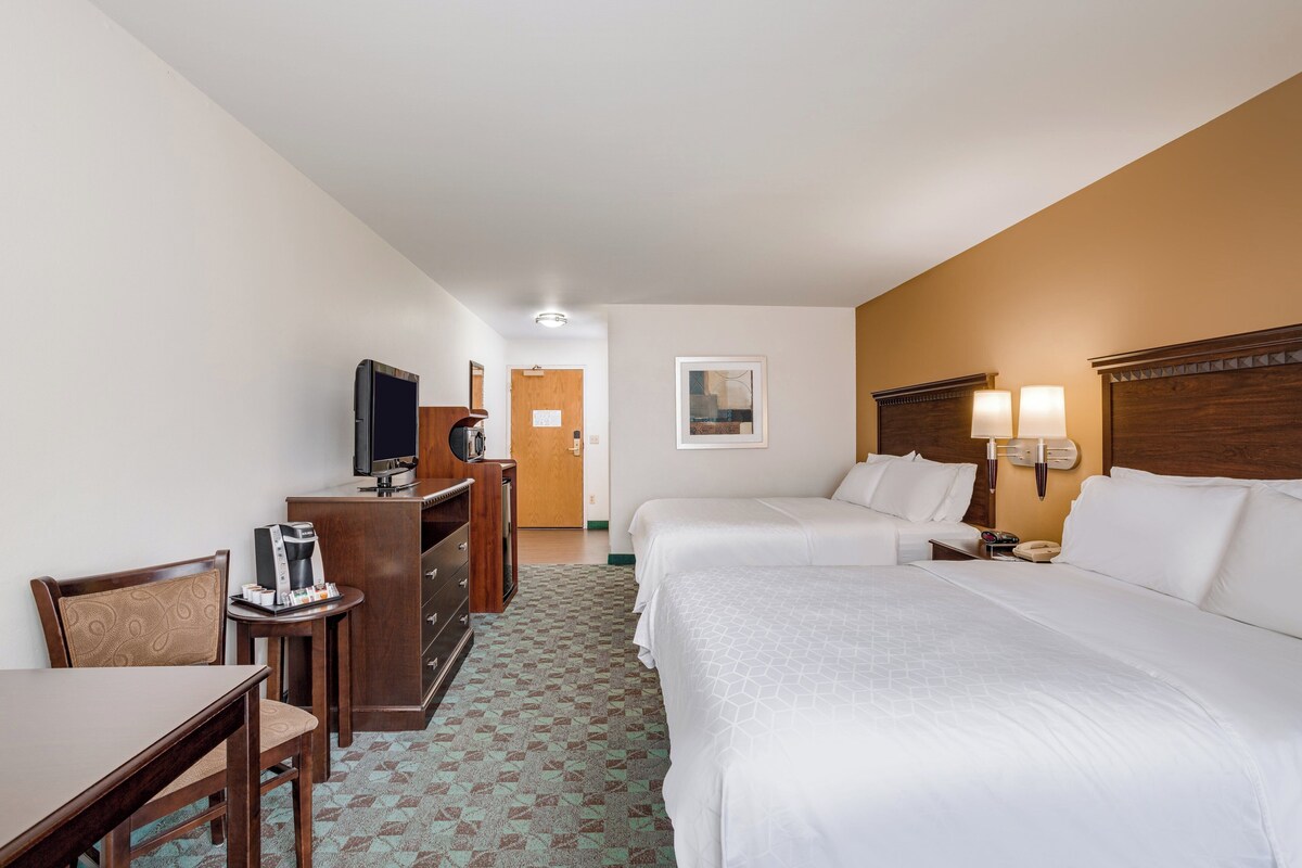 Habitación de hotel con cama, escritorio con cafetera, televisor y puerta.