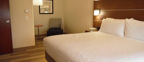 Habitación de hotel con una cama grande, una mesita de noche con una lámpara, una silla y una pequeña mesa con un teléfono y una taza.