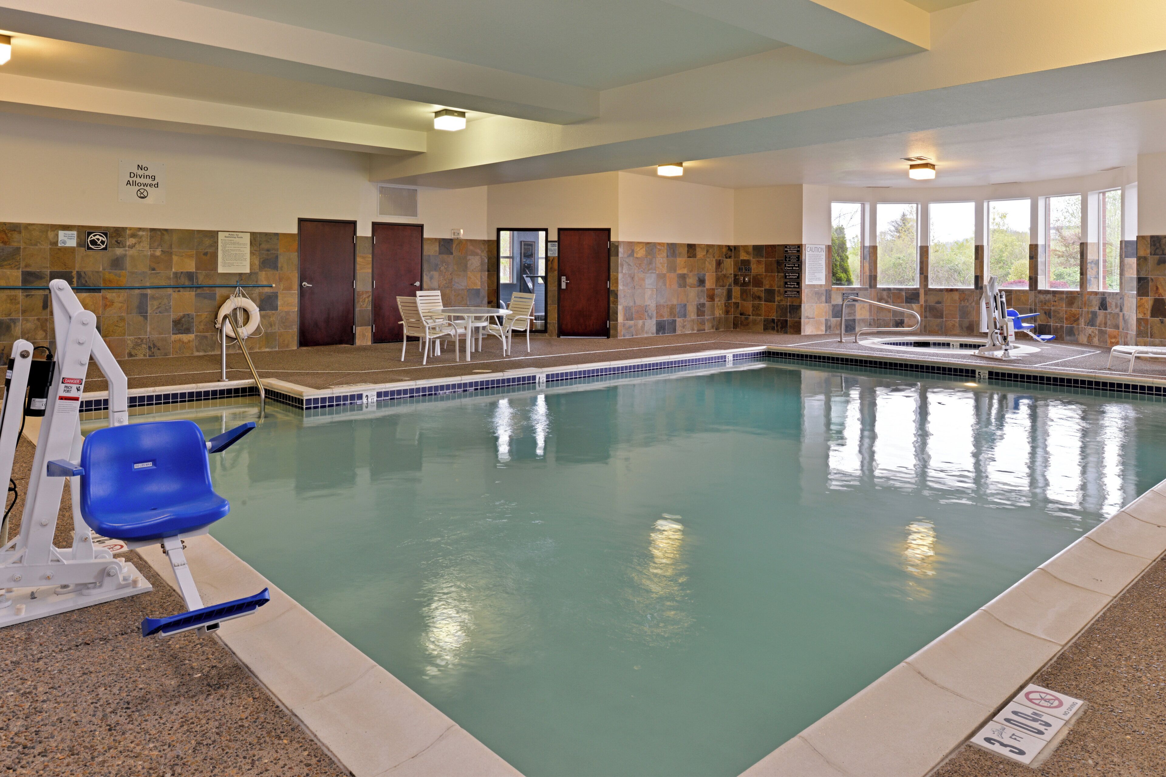 An indoor swimming pool with a lifeguard stand, chairs, and a no diving allowed sign.