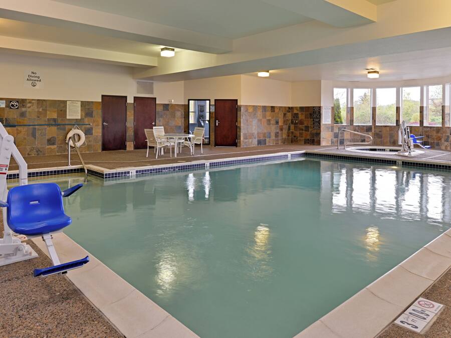 An indoor swimming pool with a lifeguard stand, chairs, and a no diving allowed sign.