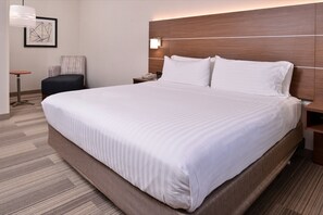 A hotel room with a large bed, a wooden headboard, a chair, a nightstand, and a framed picture on the wall. - Holiday Inn Express & Suites Albany by IHG (Albany)