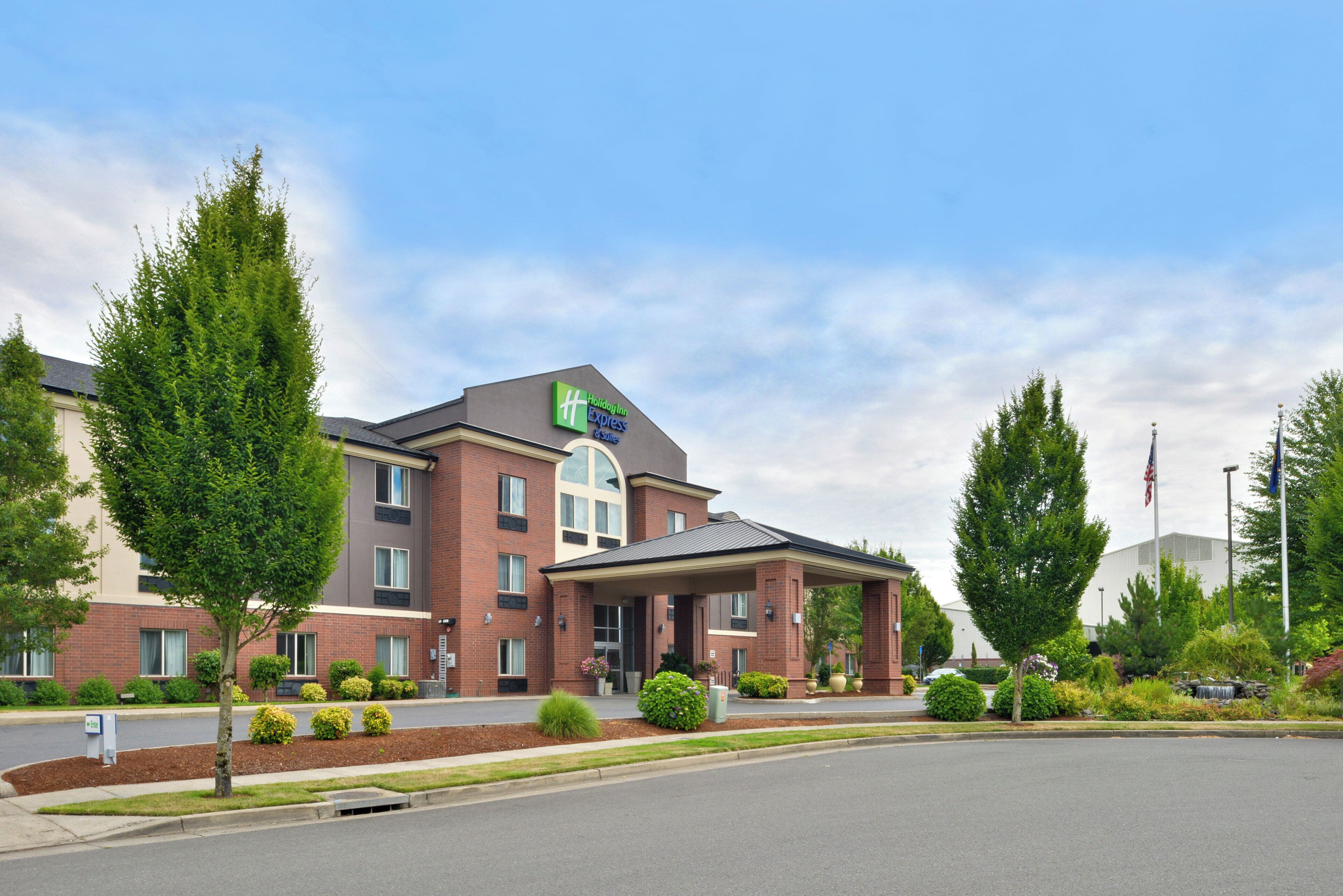 A Holiday Inn Express & Suites hotel with a brick facade, a covered entrance, and a landscaped front yard.