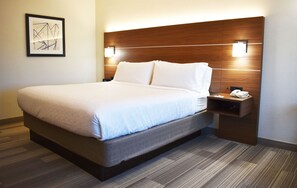 A modern hotel room with a large bed, a wooden headboard, bedside lamps, and a nightstand with a phone. - Holiday Inn Express & Suites Albany by IHG (Albany)