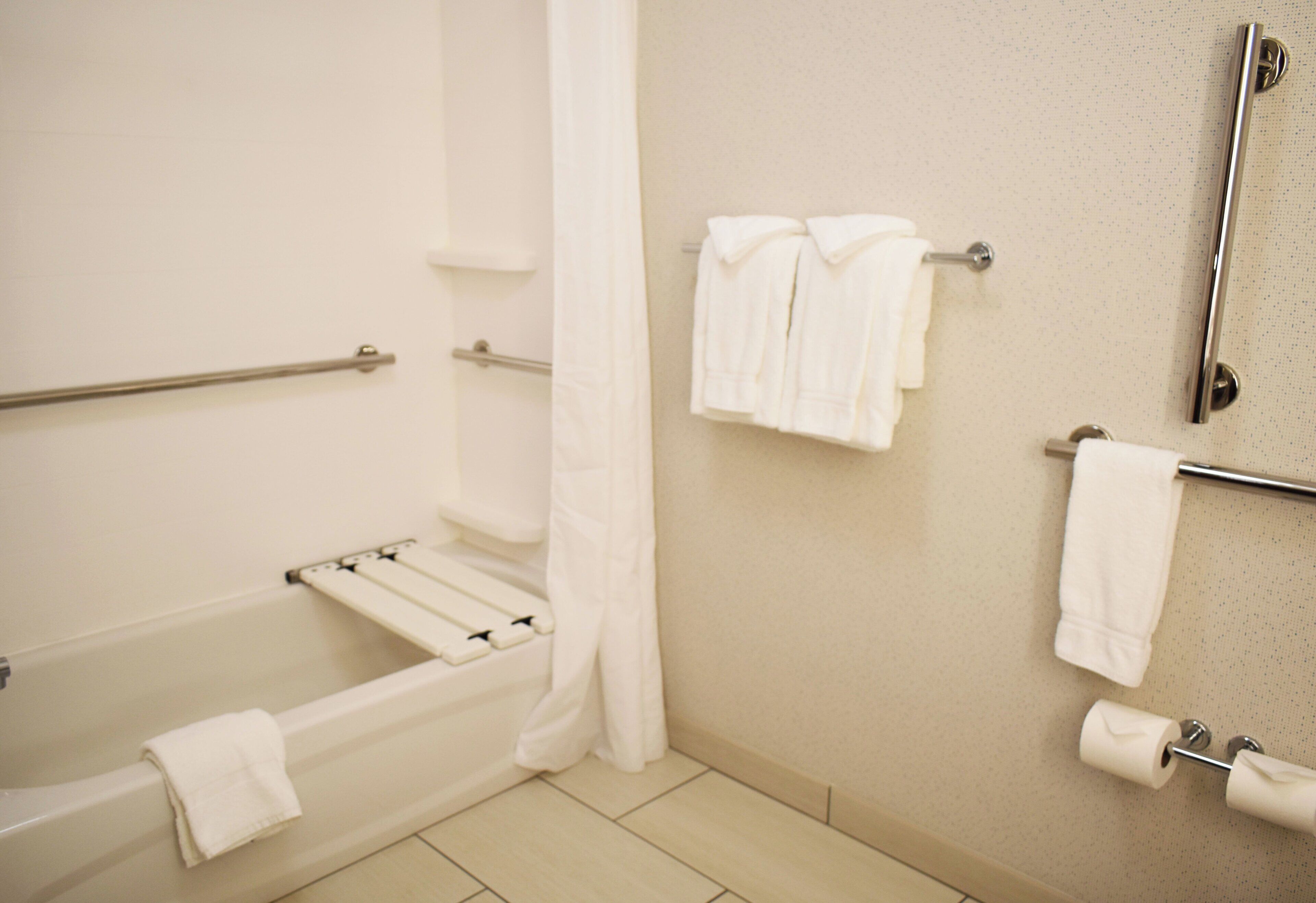 Une salle de bain équipée d’une baignoire, d’un rideau de douche, d’un porte-serviettes avec des serviettes et d’un porte-rouleau de papier toilette.