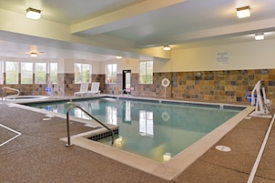 Una piscina interior con agua cristalina, paredes con azulejos y una silla para salvavidas.