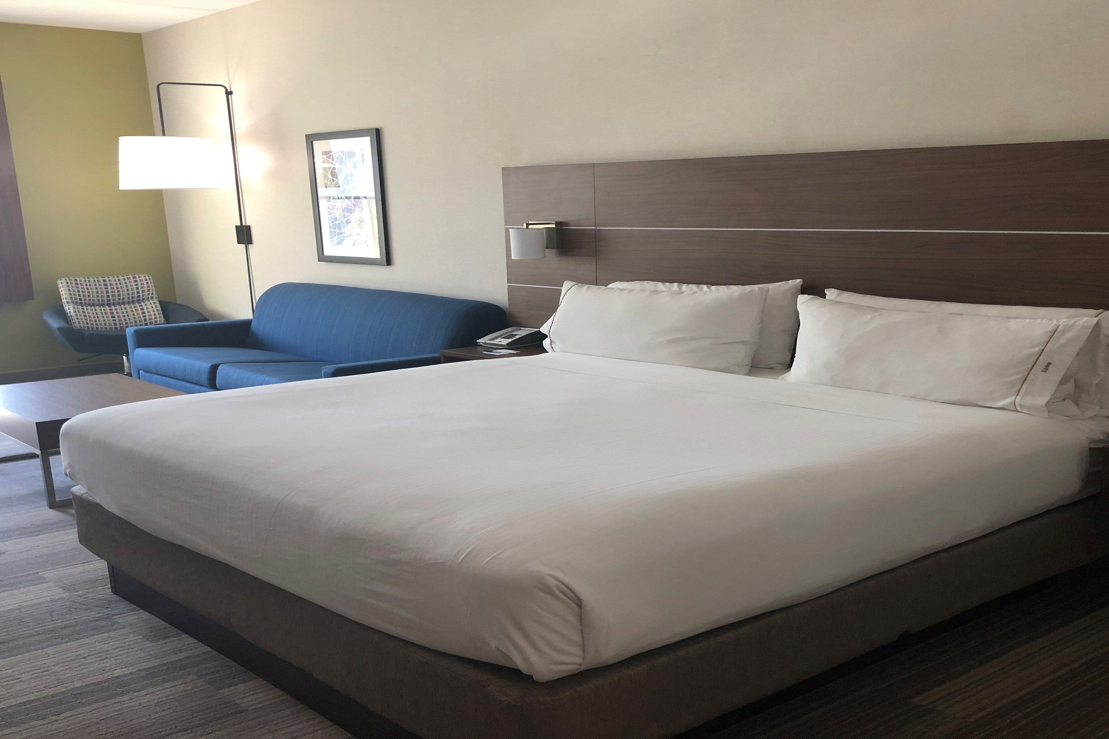 A hotel room with a large bed, a blue sofa, a bedside table, a lamp, and a framed picture on the wall.