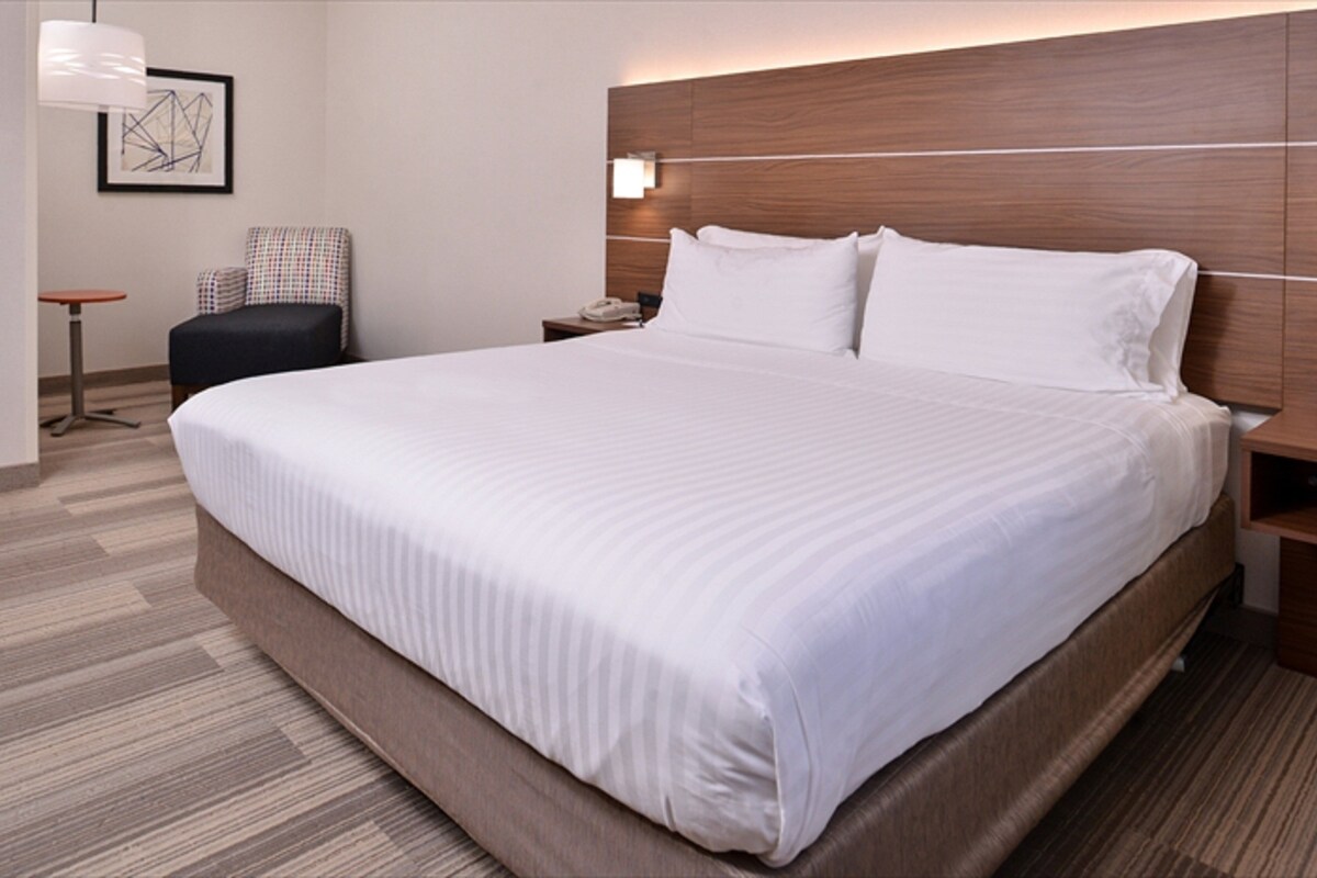 A hotel room with a large bed, a chair, a nightstand, and a wall-mounted lamp.